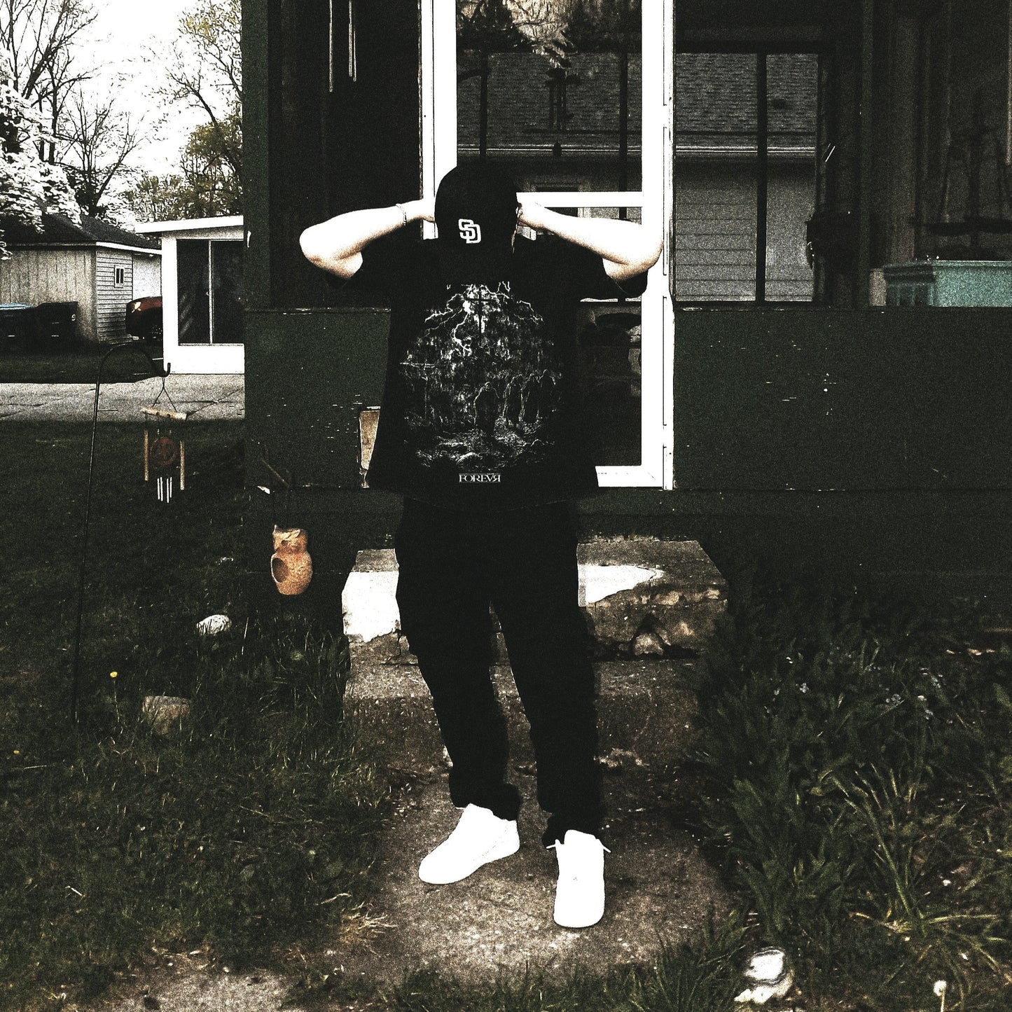 Person wearing a black hoodie with a graphic design in front of a house.