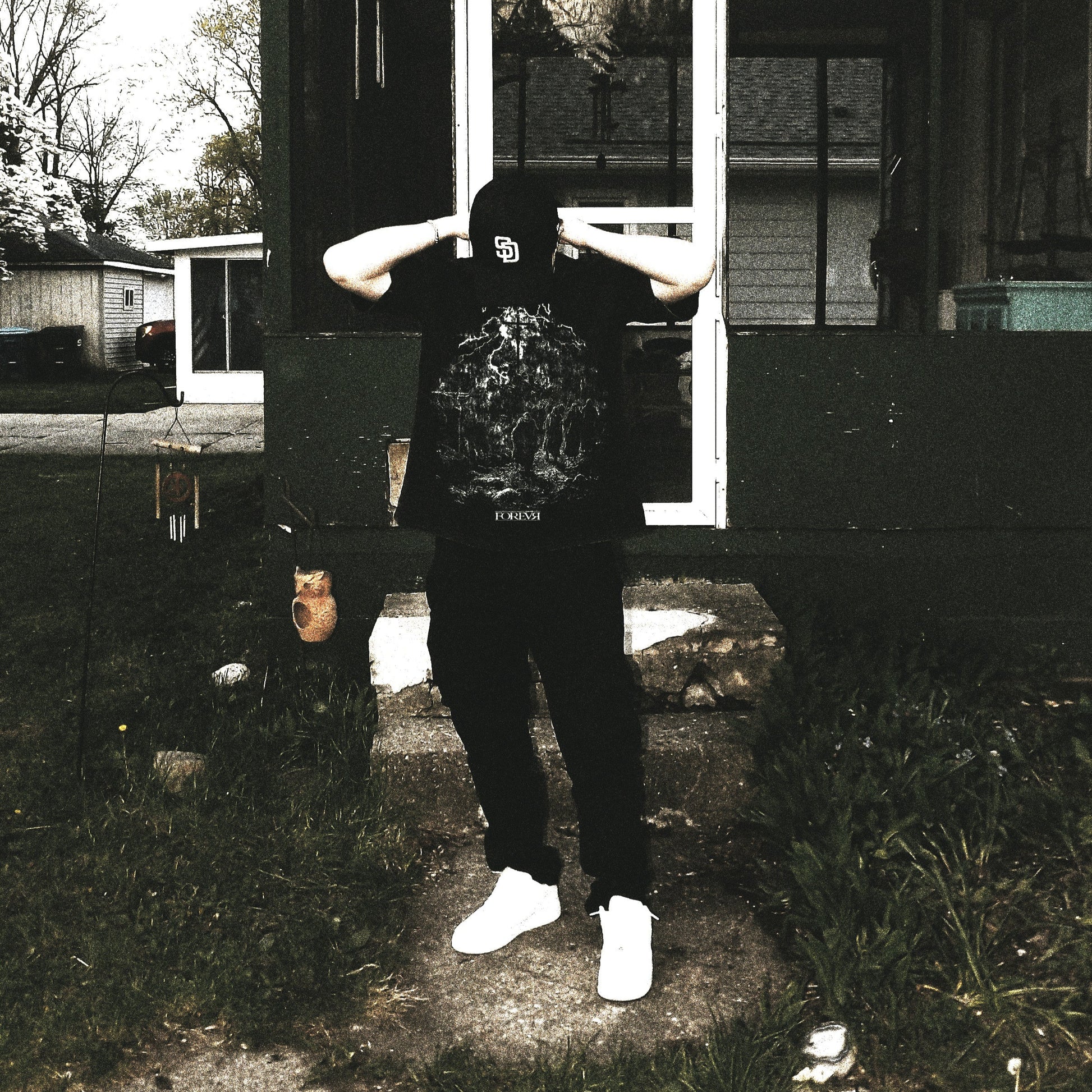 Person wearing a black hoodie with a graphic design in front of a house.