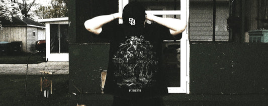 Person wearing a black hoodie with a graphic design in front of a house.