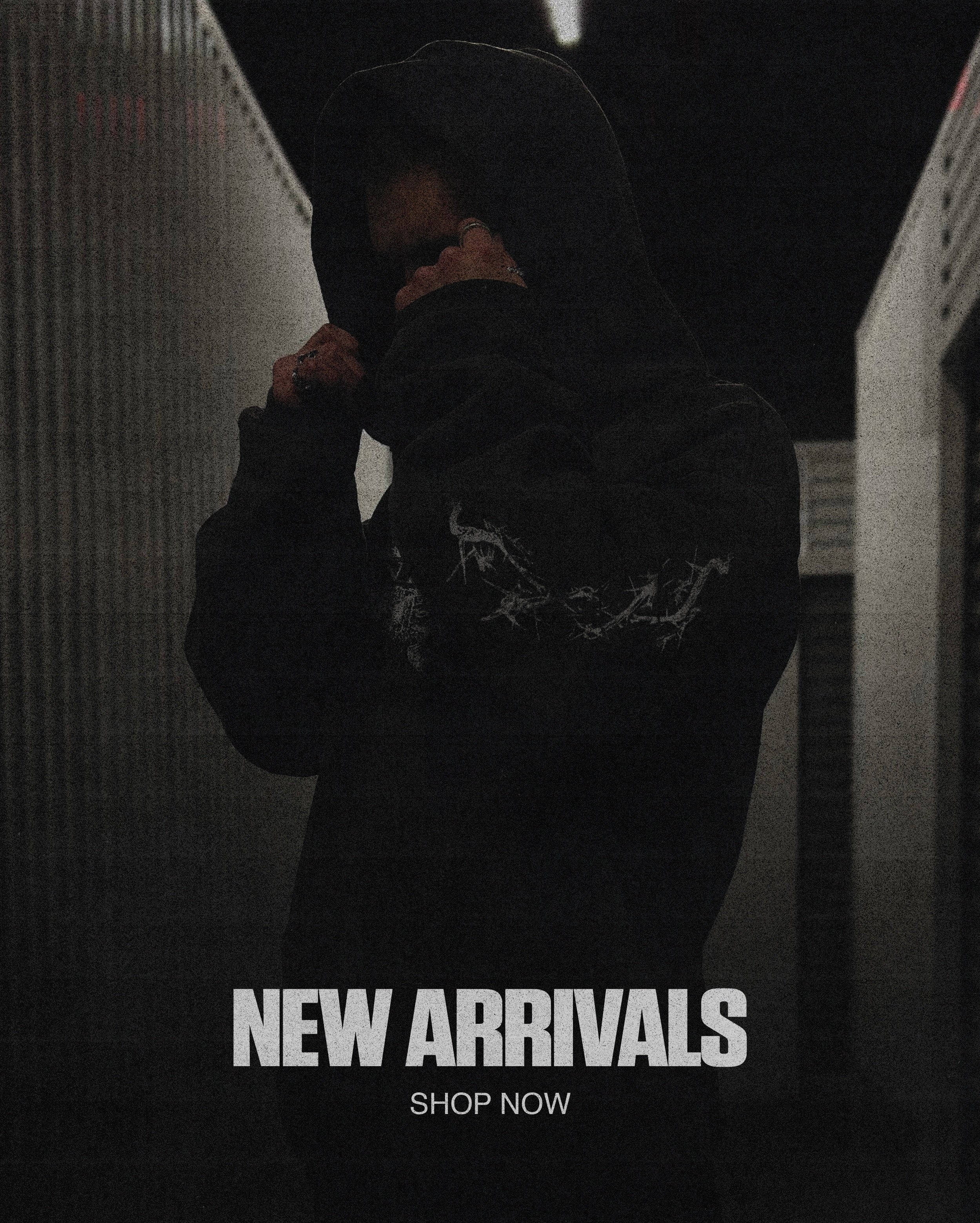 Person wearing a dark hoodie with text 'NEW ARRIVALS SHOP NOW' in a dimly lit setting.